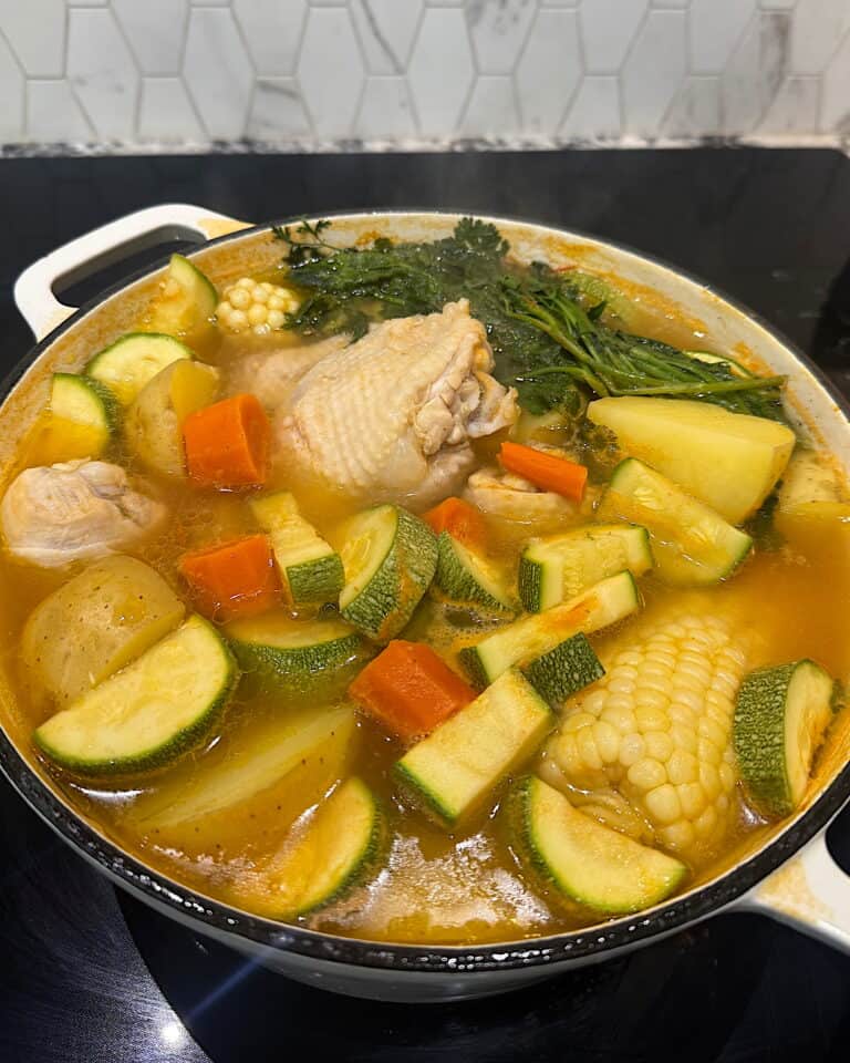 Pot of caldo de pollo with chicken, corn, carrots, potatoes, zucchini, and cilantro.