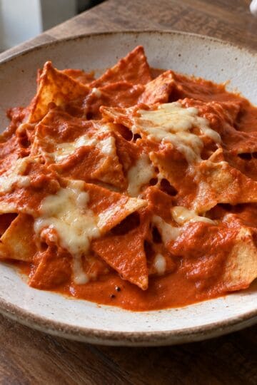 Creamy red chipotle chilaquiles with irregular tortilla pieces and melted Monterey Jack on a ceramic plate
