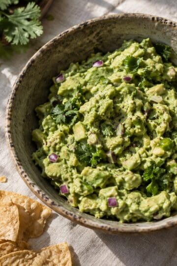 Chunky guacamole with onion, cilantro, serrano, and lime in a stoneware bowl