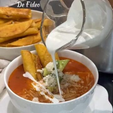 Bowl of tomato broth sopa de fideo with crema, avocado, queso fresco, and chicken taquitos