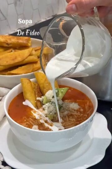 Bowl of tomato broth sopa de fideo with crema, avocado, queso fresco, and chicken taquitos