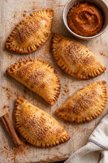 Golden baked pumpkin empanadas with fork-crimped edges and cinnamon sugar.