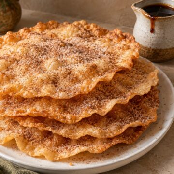Thin crisp Mexican buñuelos sprinkled with cinnamon sugar beside piloncillo syrup.