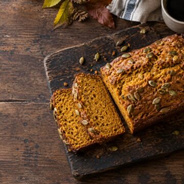 Sliced cinnamon pumpkin bread with pepitas on a wooden board