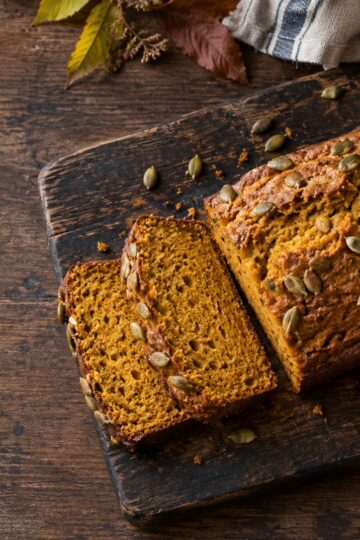 Sliced cinnamon pumpkin bread with pepitas on a wooden board