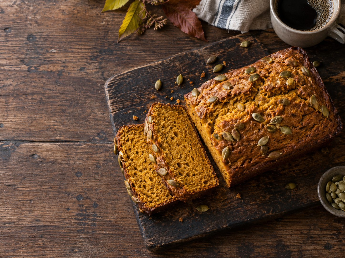 Sliced cinnamon pumpkin bread with pepitas on a wooden board